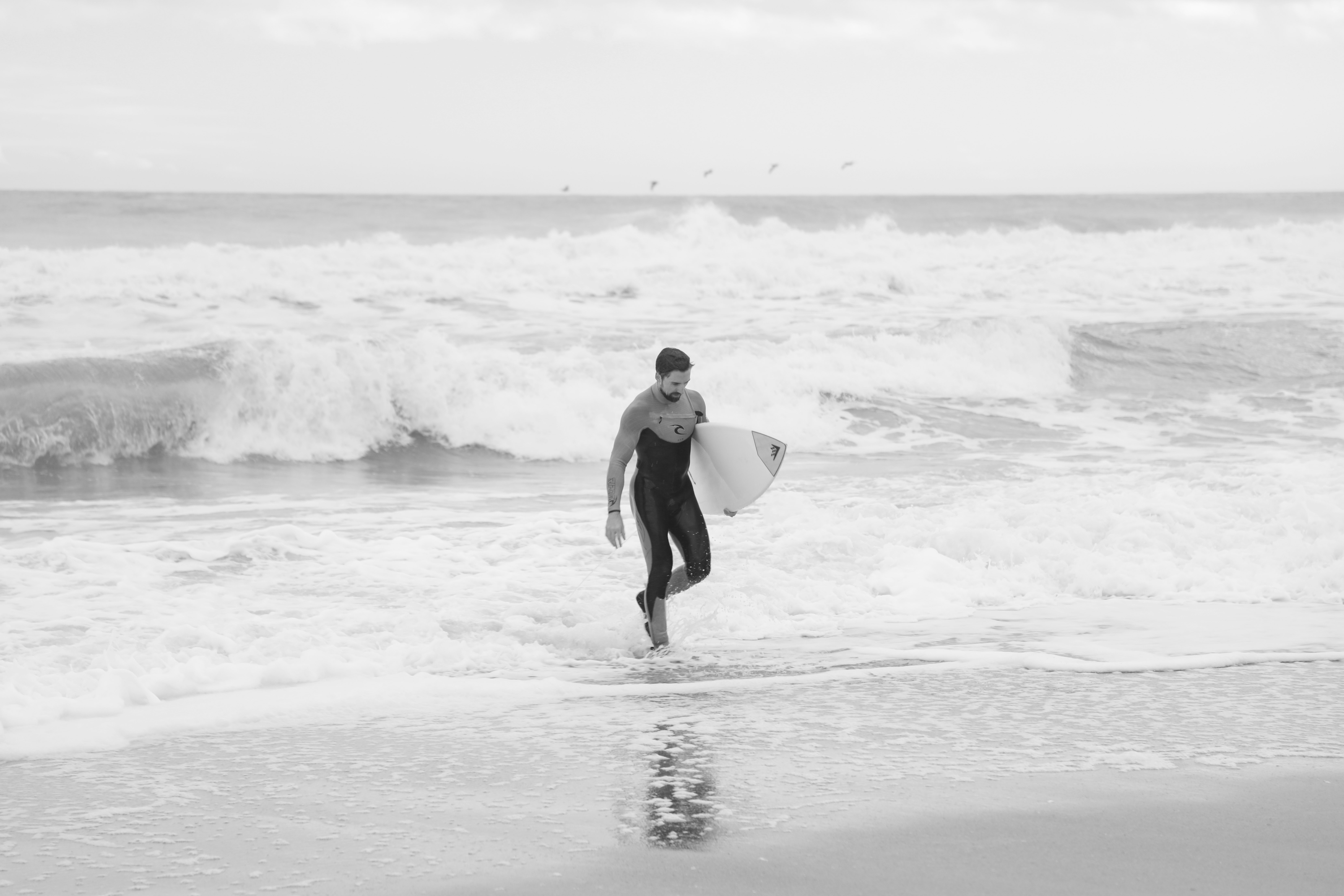 man in black wet suit holding white surfboard walking on beach during daytime